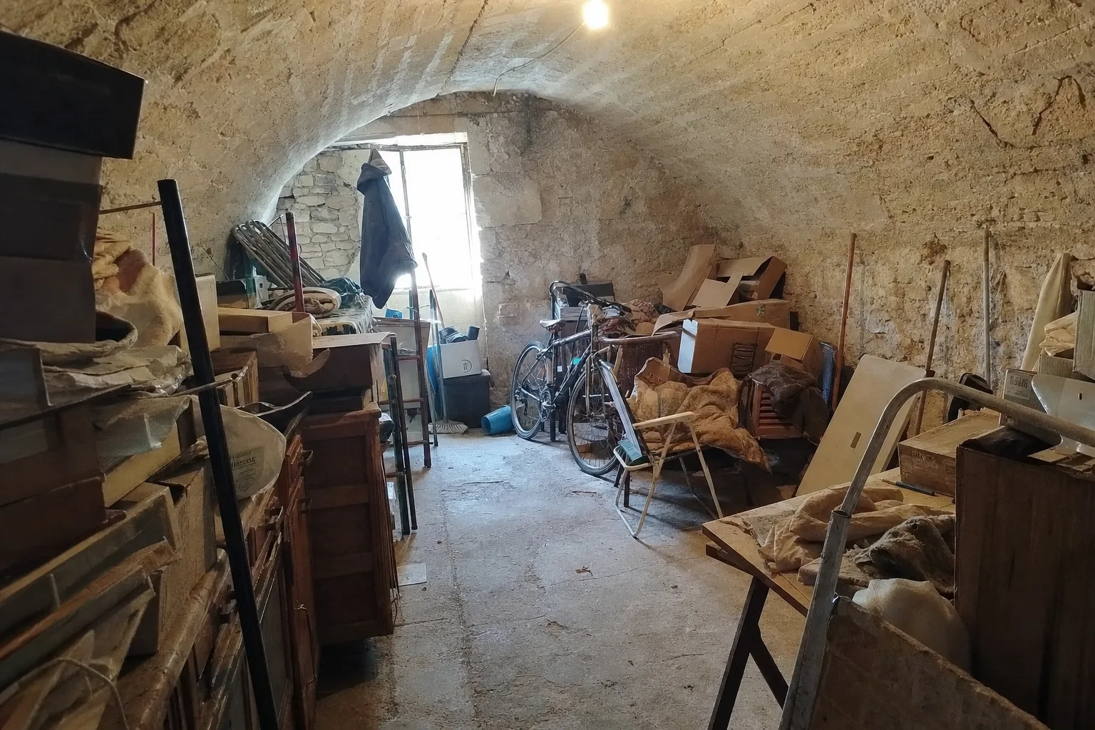 Cave en pierre encombrée de cartons, outils et vieux meubles